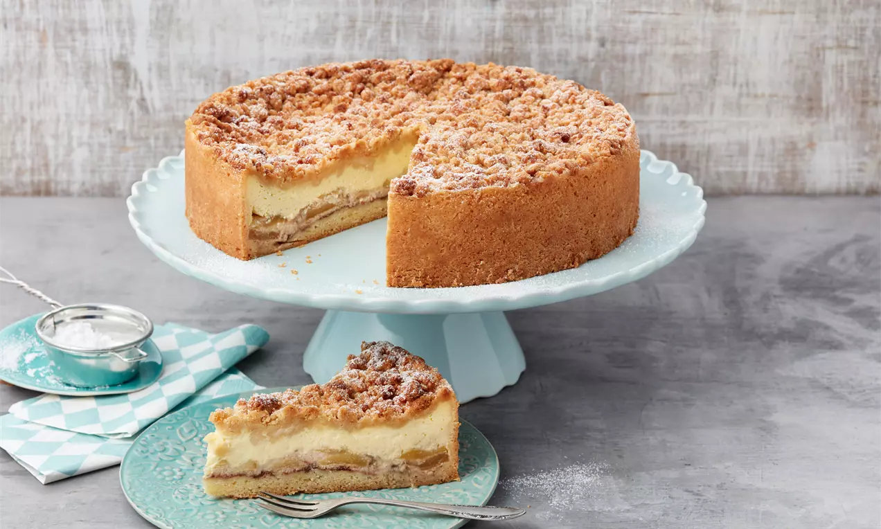Apfelkuchen mit goldbrauner Streuseldecke, cremiger Puddingfüllung und Apfelstücken, angeschnitten auf einer mintgrünen Tortenplatte