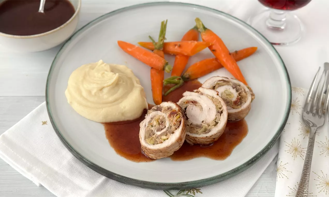 Putenröllchen mit goldbraun gebratenem Rand auf dunkler Soße, serviert mit cremigem Kartoffelpüree und glasierten Karotten auf hellem Teller