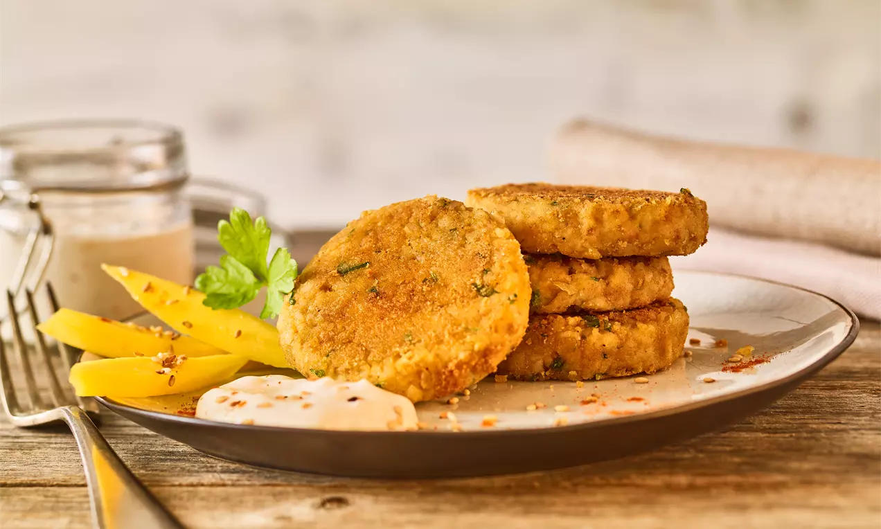 Goldbraune Gemüsebratlinge mit knuspriger Oberfläche, angerichtet auf einem Teller mit Mango-Streifen, cremigem Dip und Petersilie