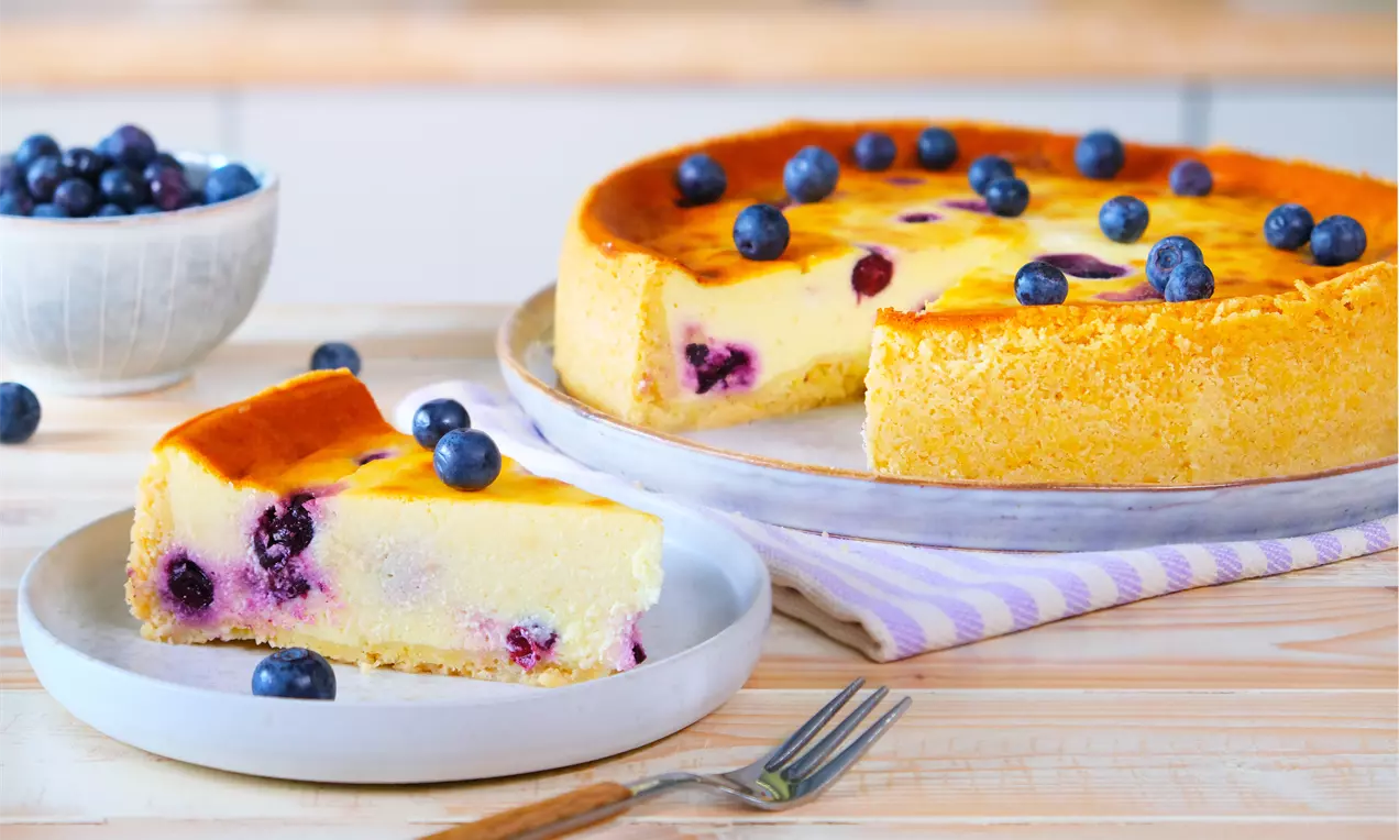 Goldgelber Skyr-Kuchen mit saftigen Blaubeeren, cremiger Textur und leicht gebräunter Oberfläche auf Tellern mit lilierter Serviette drapiert