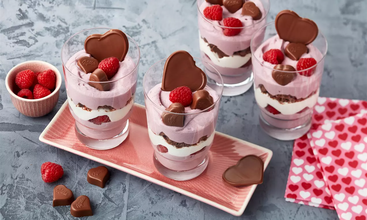Cremiges Valentinstag-Dessert mit samtiger Rotweincreme, frischen roten Himbeeren und Minzblatt auf weißem Dessertteller