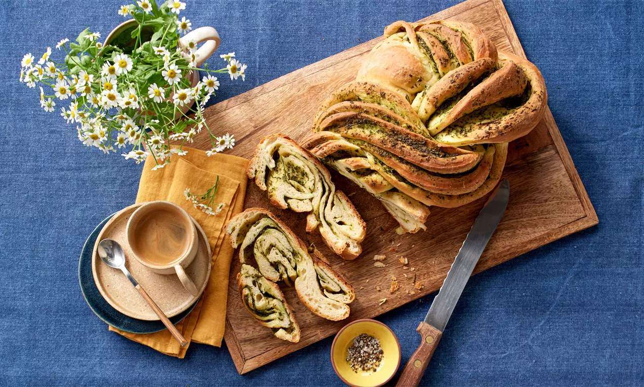 Kräuterbrot mit goldbrauner Kruste, aufgeschnitten, buttrig-weiche Schnittflächen mit grünen Kräuterflecken, auf Holzbrett serviert