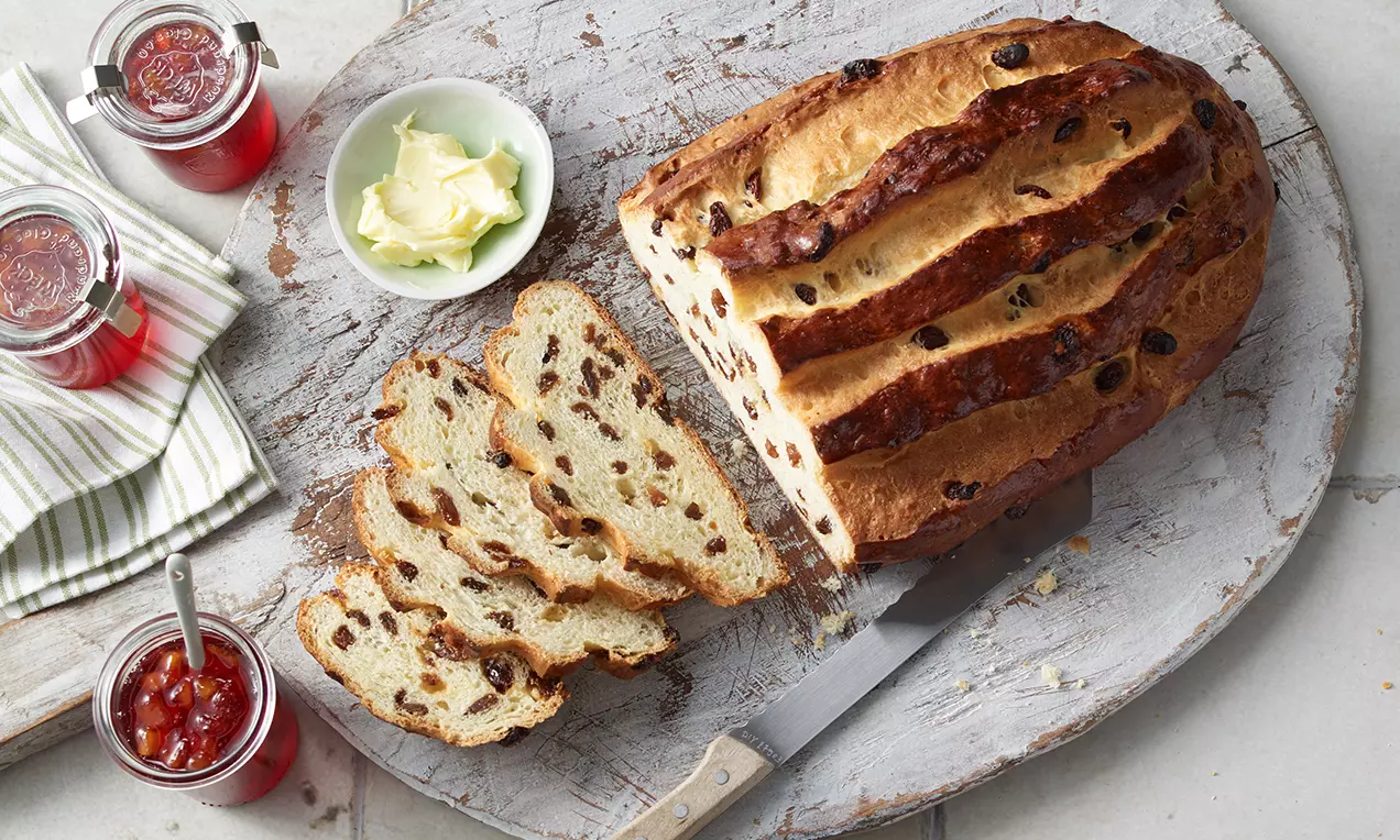 Rosinenbrot mit goldbrauner Kruste, aufgeschnittene Scheiben zeigen fluffiges helles Inneres mit saftigen Rosinen, serviert auf Holzbrett