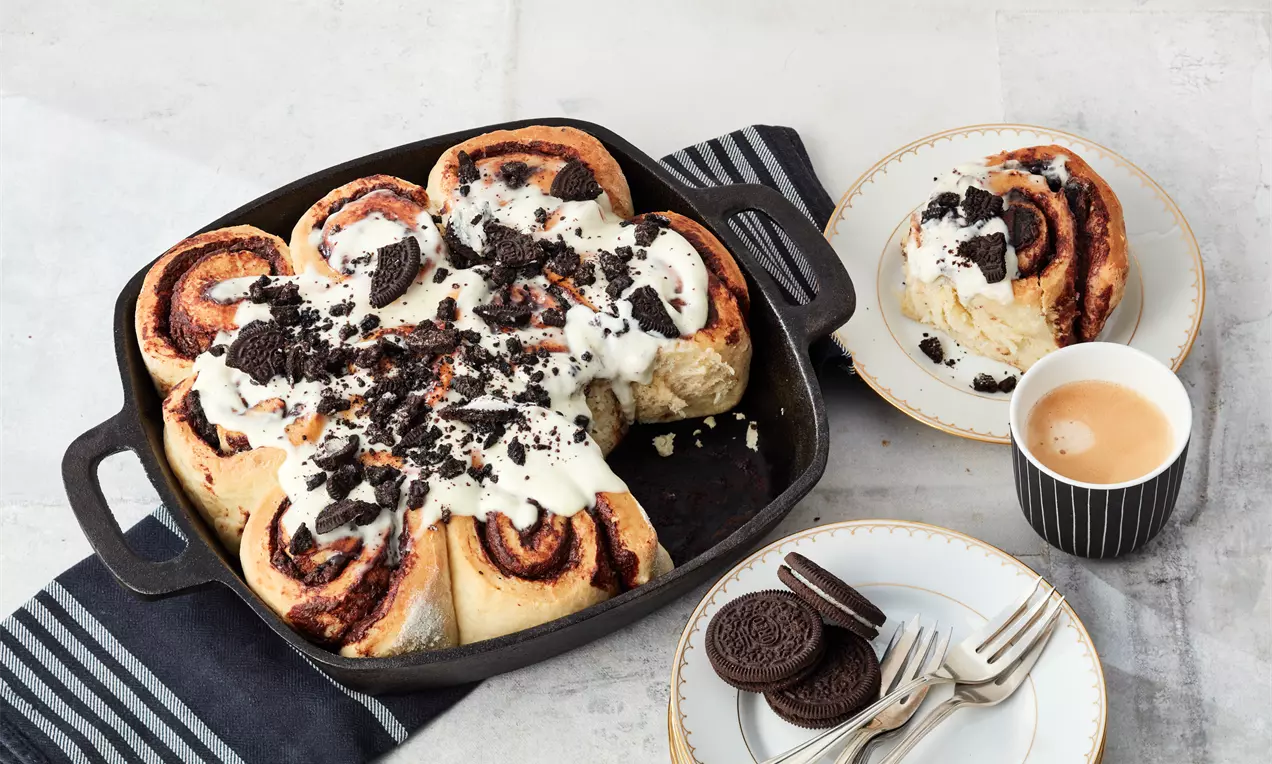 Gedrehte Hefeteigrollen mit dunkler Oreo®-Füllung, bedeckt mit weißer Glasur und zerbröselten Oreo®-Stücken in einer schwarzen Servierpfanne