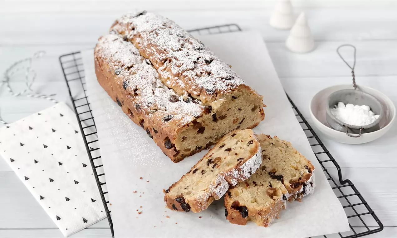 Quark-Christstollen goldbraun mit Puderzucker bestäubt, mit eingebackenen Rosinen und Mandeln auf Backpapier auf einem Kuchengitter