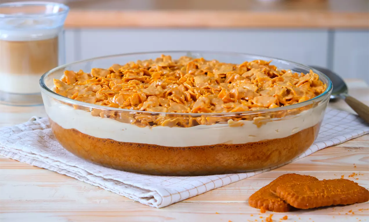 Lotus Crunch Dessert mit Karamell-Keksboden, cremiger Füllung und knusprigem Topping in einer klaren Glasform auf weißem Tuch