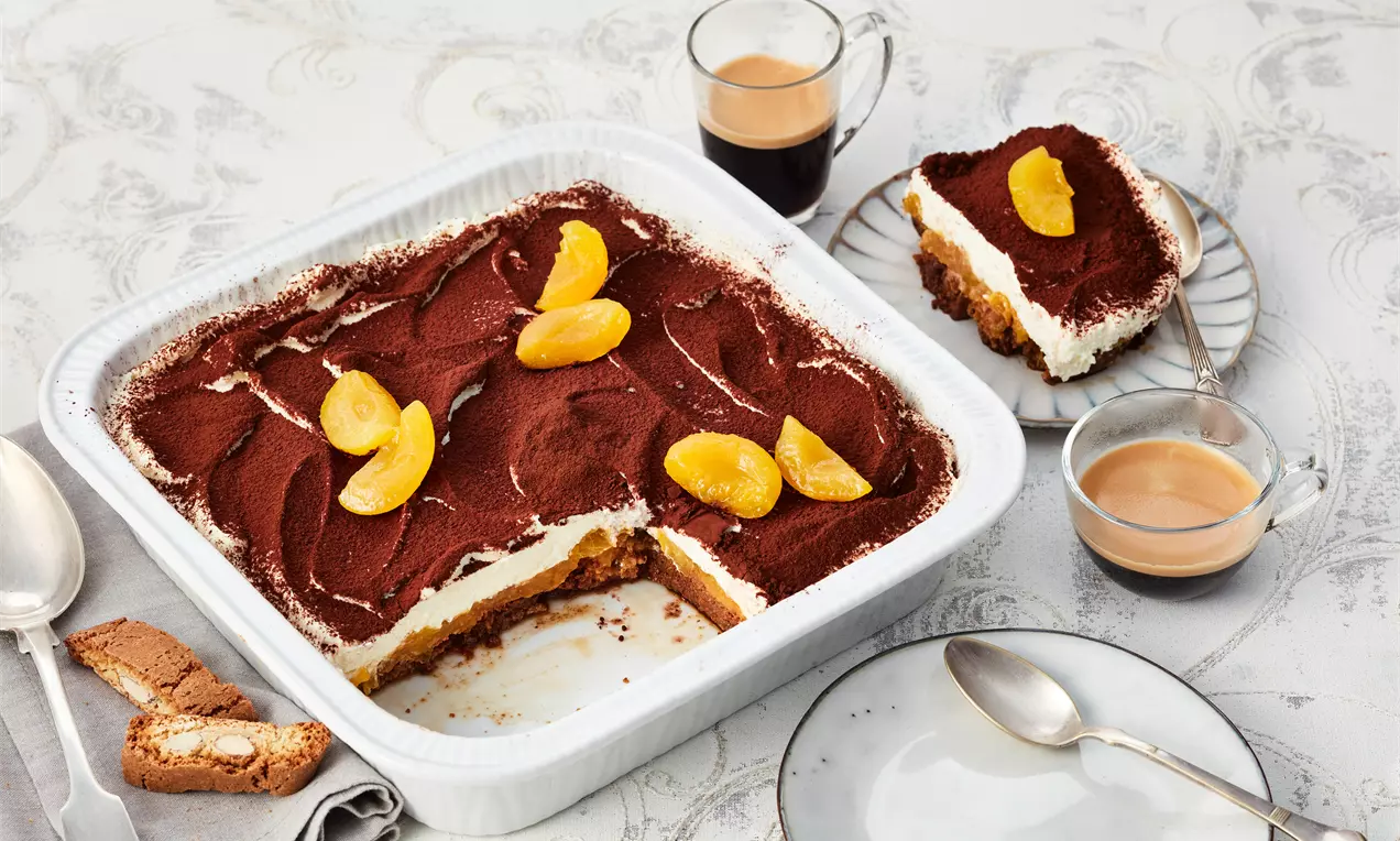 Aprikosen-Tiramisu mit weißer Creme und dunklem Kakao auf lockerer Schicht in quadratischer Form, dekoriert mit gelben Aprikosenspalten