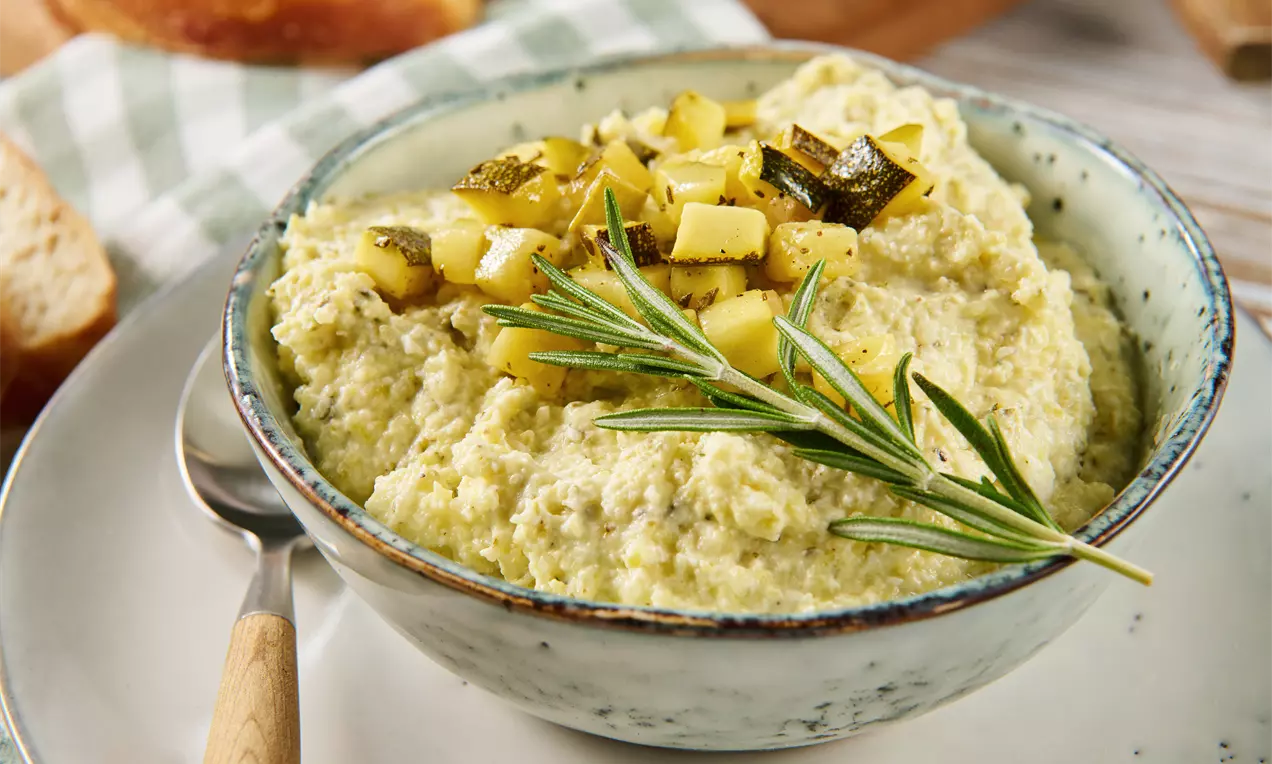 Cremiger Zucchini-Dip in einer gesprenkelten Schale, mit goldbraun angebratenen Zucchiniwürfeln und frischem Rosmarinzweig garniert