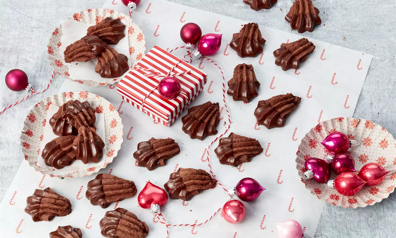 Schokoladenbraune Bärentatzen mit geriffelten Konturen, teils in Papierförmchen, arrangiert auf weißem Untergrund mit roten Weihnachtskugeln