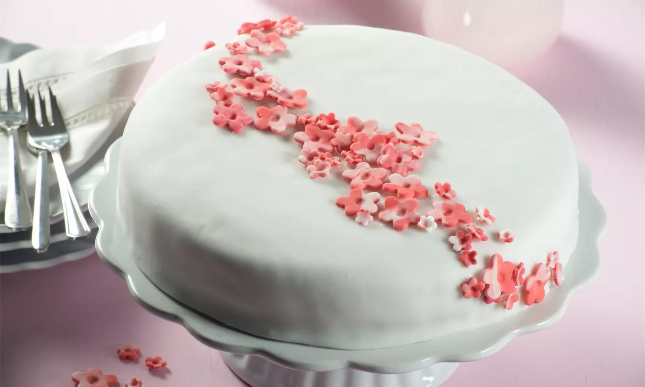 Weiße Canache-Torte auf gewelltem Tortenständer, diagonal mit marmorierten rosa und roten Blüten dekoriert
