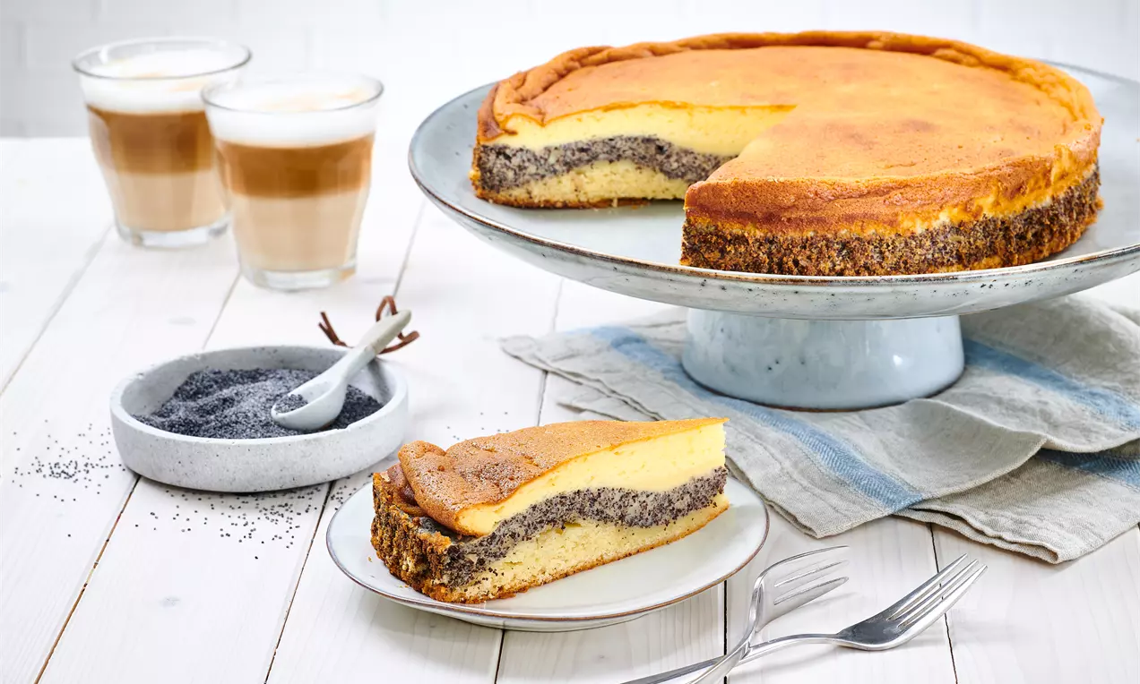 Thüringer Mohnkuchen mit goldgelber Käsekuchenschicht und dunkler Mohnfüllung auf silberner Tortenplatte, daneben ein Stück auf einem Teller
