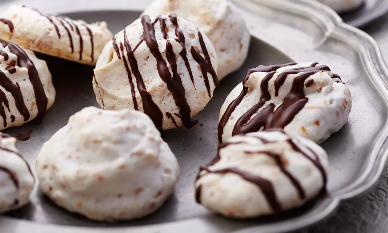 Kokosmakronen mit heller, leicht gerösteter Oberfläche und dunklem Schokoladen-Dekor auf einem silbernen Teller angerichtet