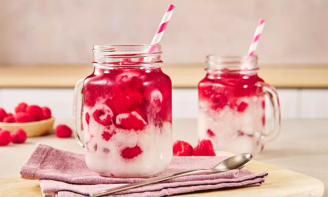 Ein rosafarbenes Getränk mit frischen Himbeeren, marmorierten weißen Schichten und gestreiftem Trinkhalm in einem klaren Henkelglas