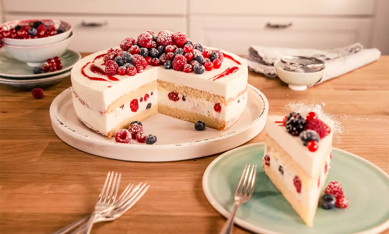 Beerige Käse-Sahne-Torte mit weißer Creme auf hellem Boden und roten sowie blauen Beeren, leicht bestäubt auf einer weißen Platte