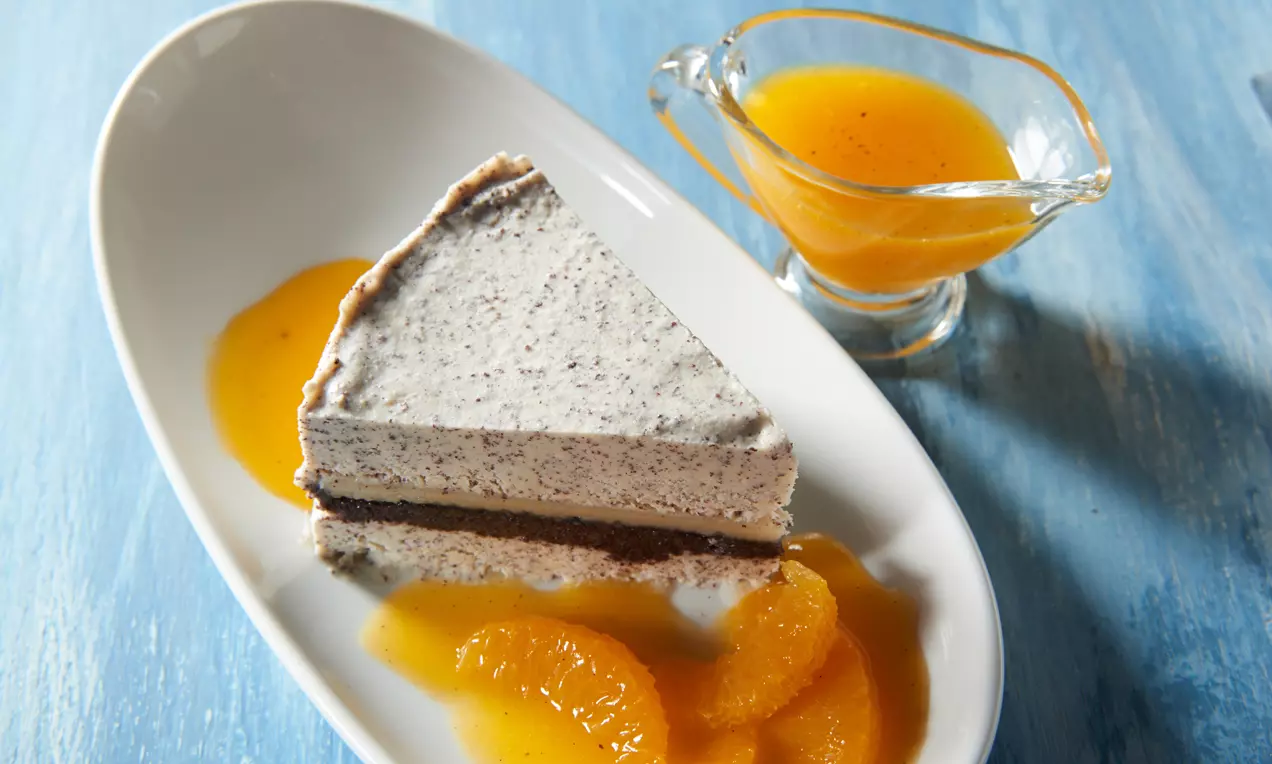 Dreieckiges Mohn-Marzipaneis mit feinen grauen Punkten, Orangensoße und fruchtigen Orangenfilets auf weißem Teller mit Dekorsoße