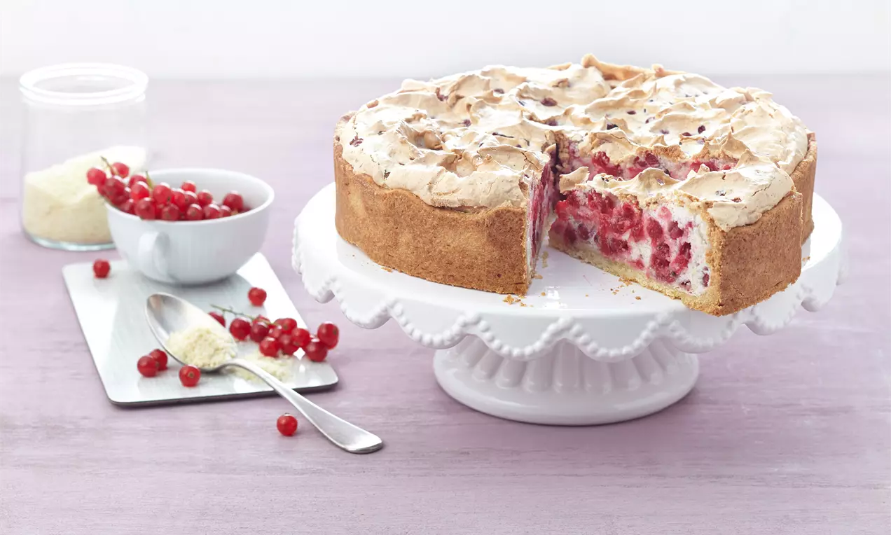 Johannisbeer-Baiser-Torte mit goldbraunem Rand, weißer Baiserhaube und roter Beerenfüllung auf einer verzierten weißen Tortenplatte