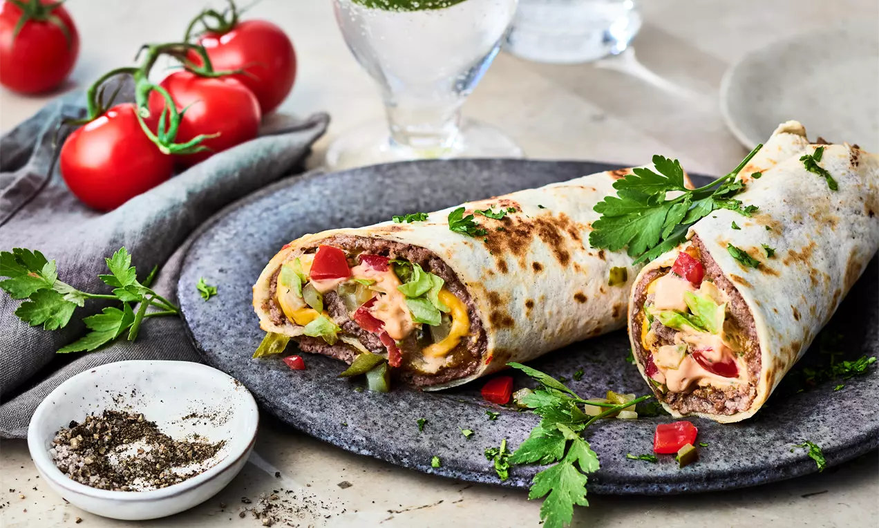 Zwei längliche, goldbraun gebratene Wraps mit bunter Gemüsefüllung, angerichtet auf dunklem Teller, garniert mit frischen Kräutern
