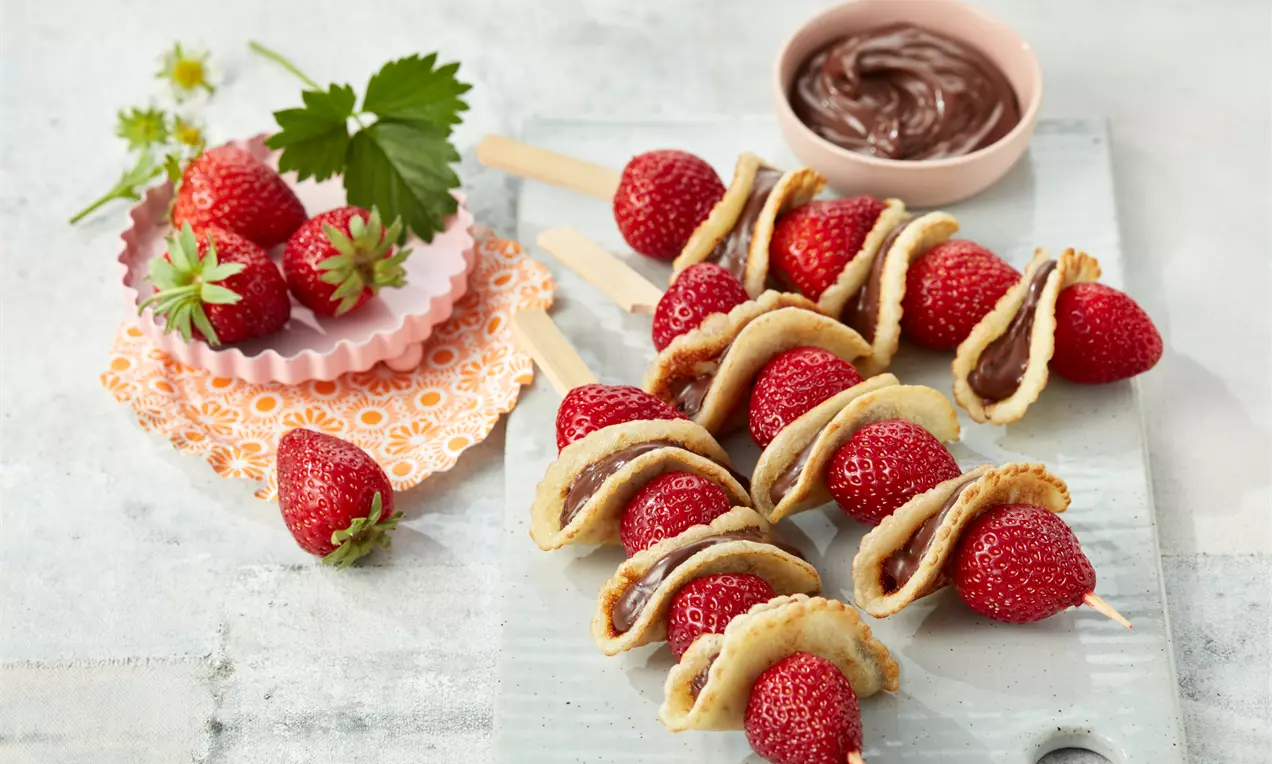 Erdbeer-Püfferchen-Spieße mit leuchtend roten Erdbeeren und goldbraunen Mini-Pfannkuchen, gefüllt mit Nutella auf Holzspießen angerichtet