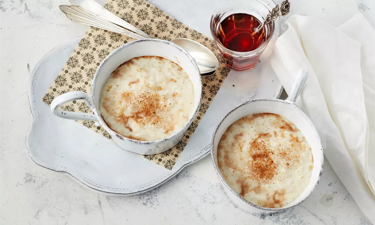 Türkischer Milchreis mit heller, cremiger Oberfläche, goldbrauner Zimtschicht in weißen Schalen auf einem Tablett mit Tee und Besteck
