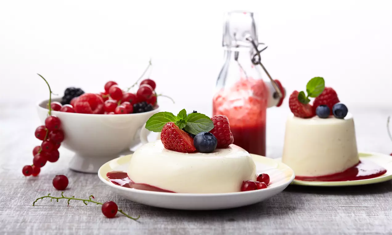 Panna cotta mit glatter, weißer Oberfläche auf Beerensoße, dekoriert mit frischen Beeren und Minze, serviert auf einem Teller