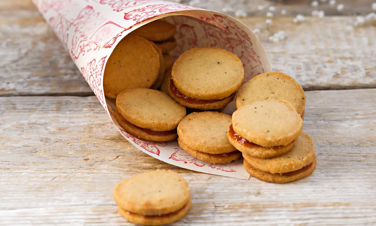 Plätzchen mit Hagebuttenmarmelade: goldbraune Marzipanplätzchen mit leuchtend roter Füllung, bestäubt mit Puderzucker auf Teller