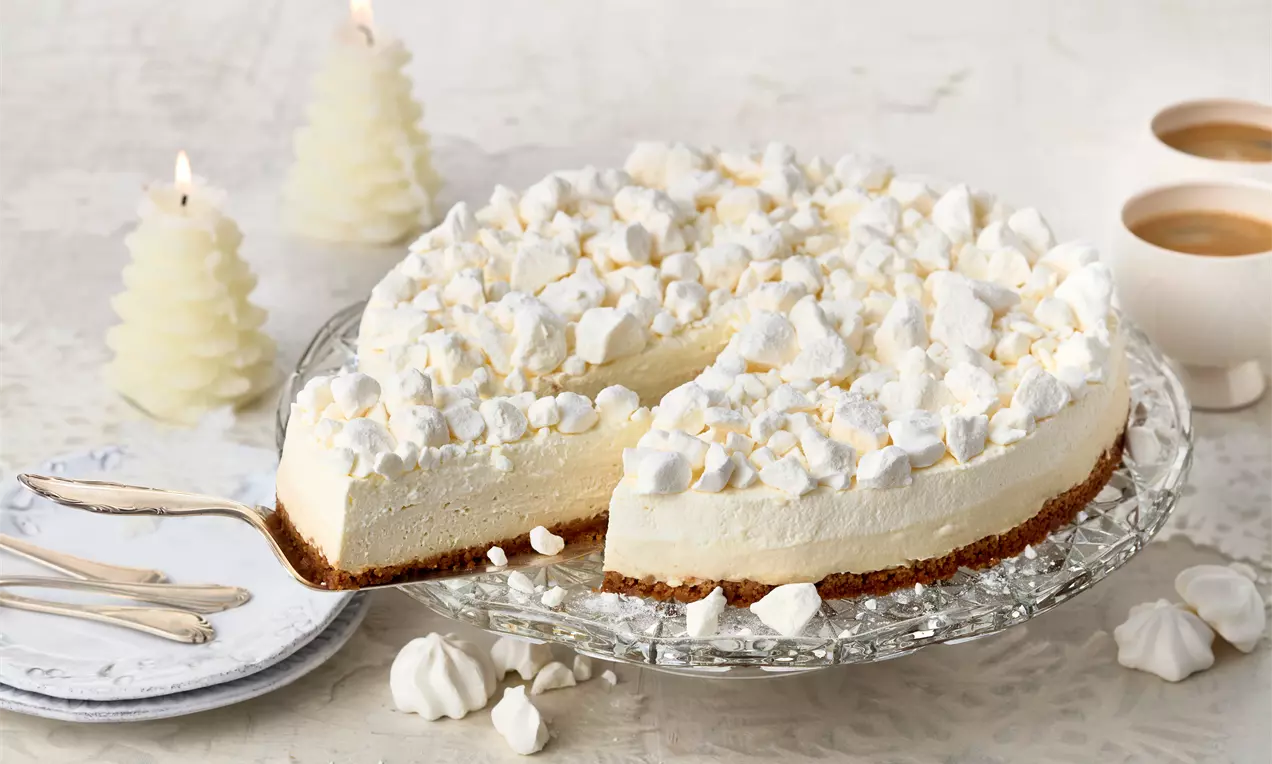 Schneeflöckchen-Torte mit weißer Sahnecreme und zarten Baiser-Stücken auf knusprigem Keksboden, serviert auf Glasplatte mit Kerzen-Dekoration