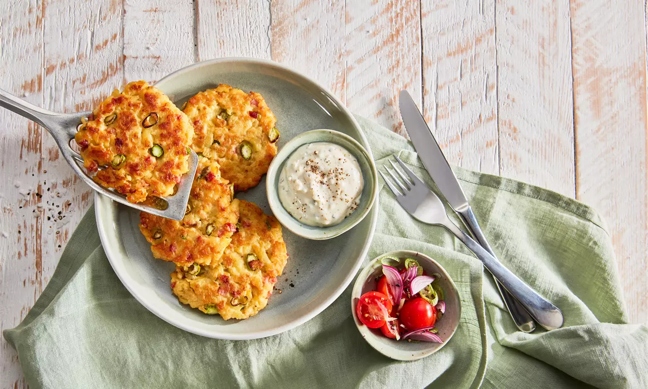 Goldene, knusprige Spargelrösti mit grünen Spargelstücken auf einem hellen Teller, serviert mit Dip und einem Beilagenschälchen