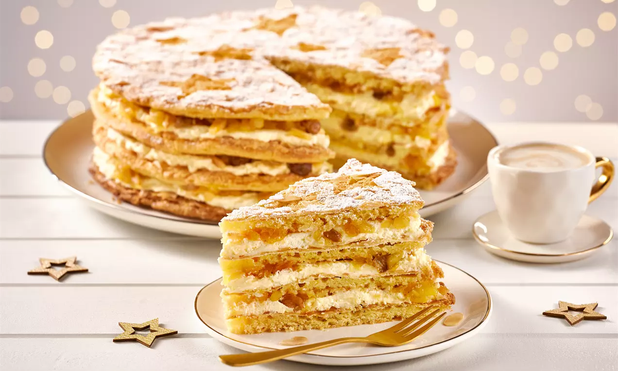 Mehrschichtige Himmelstorte mit goldbraunem Mürbeteig, Sahne und Fruchtfüllung, bestäubt mit Puderzucker, serviert auf einem Teller mit Gabel
