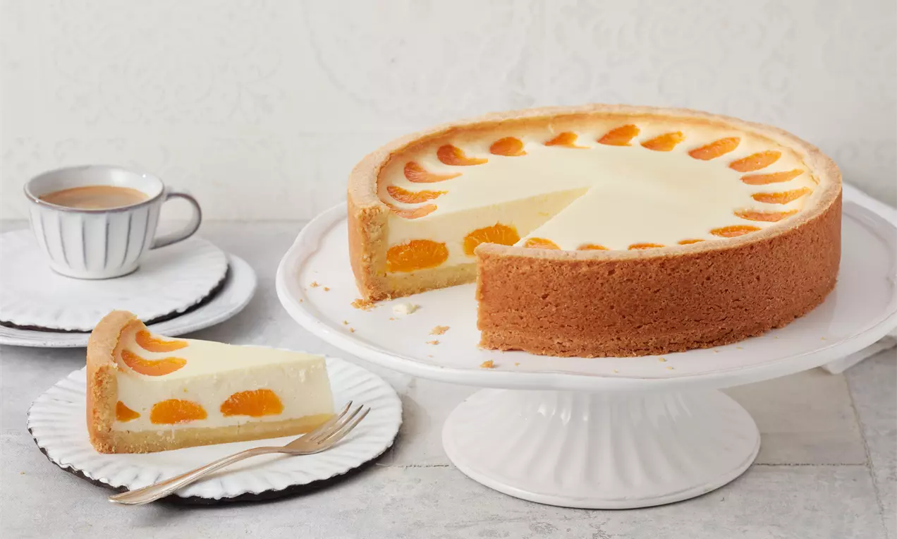 Käsekuchen mit Mandarinen mit cremig-heller Füllung, leicht gebräunter Kruste, glänzenden orangefarbenen Mandarinenfilets obenauf