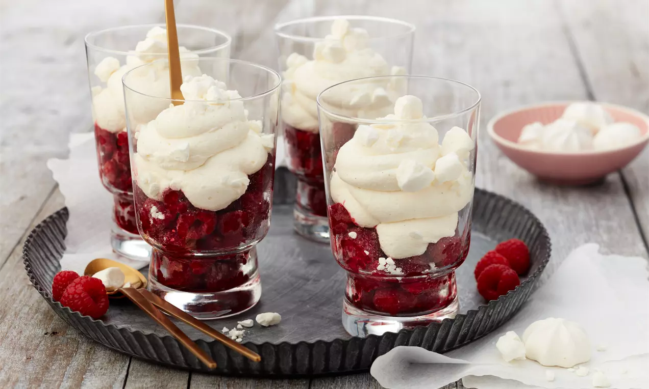 Schneegestöber im Glas mit fluffiger weißer Creme, schichtweise tiefroten Himbeeren und zarten, hellen Baiserbröseln garniert