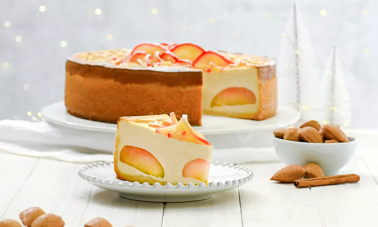 Ein Stück Bratapfel-Käsekuchen mit cremiger Füllung, sichtbaren Apfelstücken und Mandelsplittern auf einem weißen Teller angerichtet