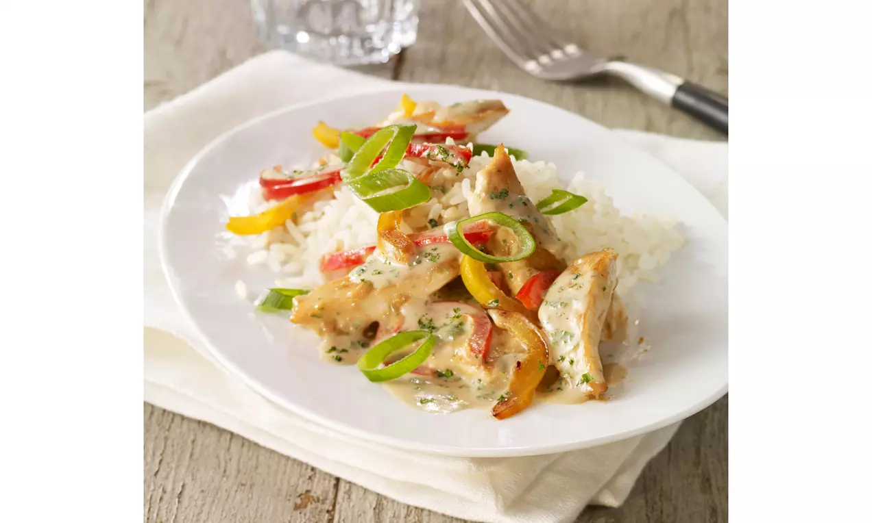 Buntes Hähnchengeschnetzeltes mit zarten Hähnchenstreifen, leuchtend orange Möhren, grüner Lauch und gelber Mais in cremiger Sauce auf Teller