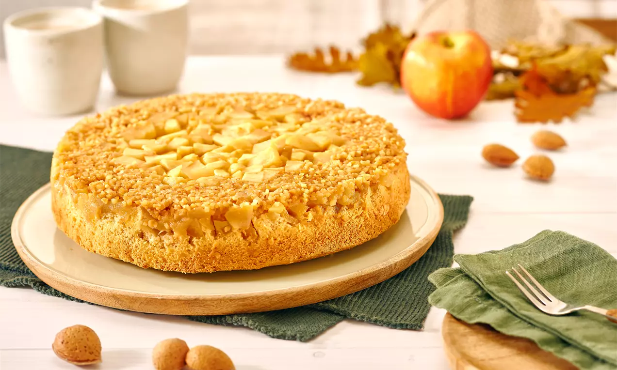 Goldbrauner gestürzter Apfelkuchen mit karamellisierten Apfelstücken und knuspriger Kruste auf einem Teller, umgeben von herbstlicher Dekoration