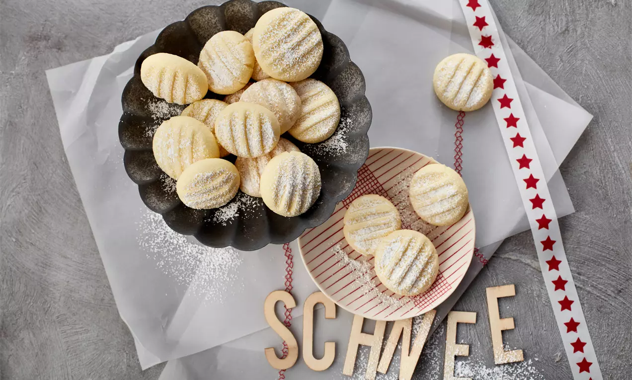 Schneeflöckchen: zarte, goldbraune Plätzchen mit weißem Puderzucker, sternförmig ausgestochen und auf Holzbrett arrangiert