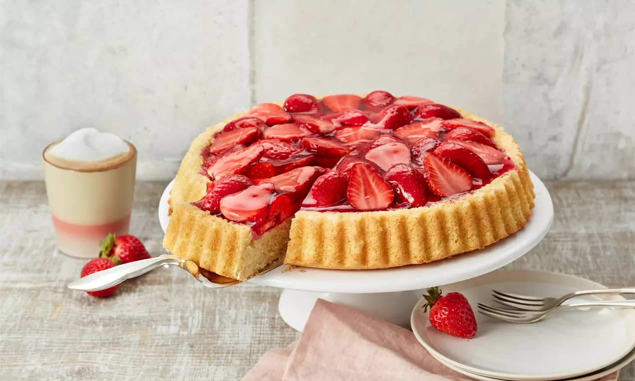 Erdbeerkuchen mit glänzenden roten Erdbeeren, hellem Biskuitboden und zartem Tortenguss, dekoriert mit Minzblatt
