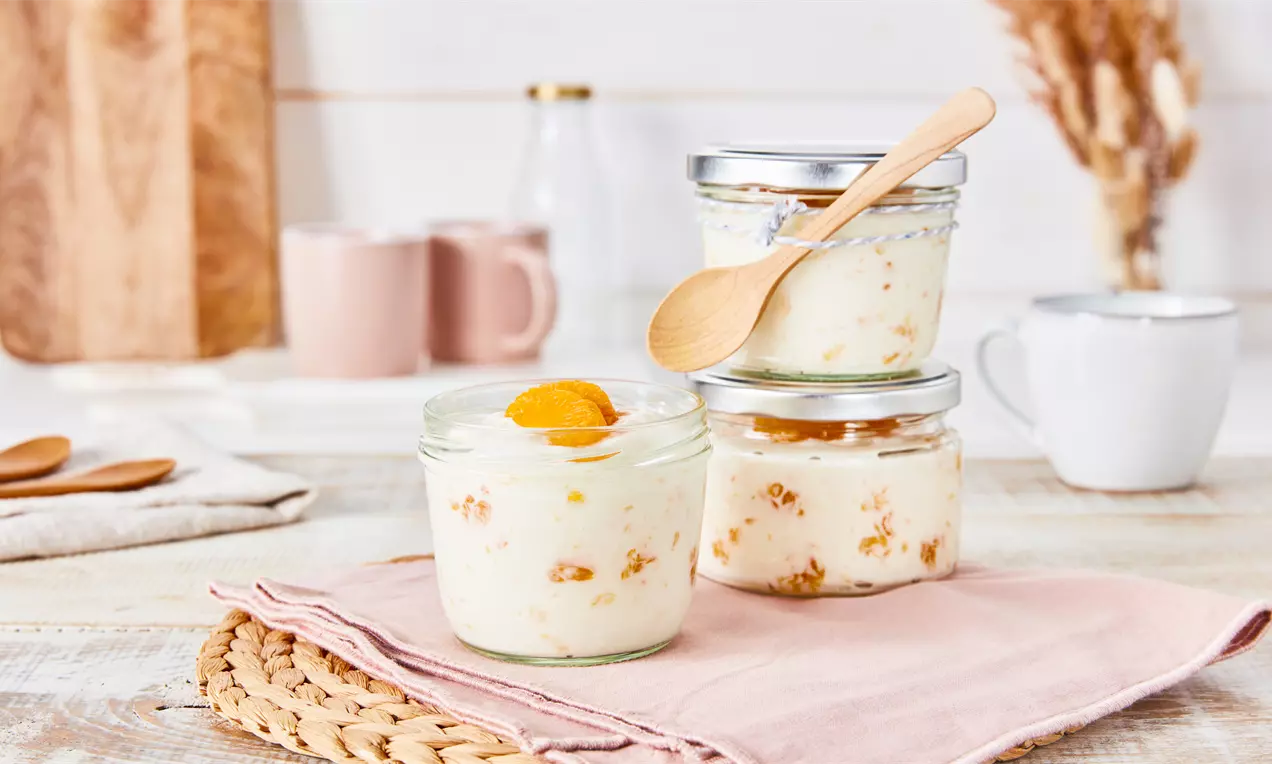 Käse-Sahne-Creme mit heller, cremiger Textur und Mandarinenstücken in klaren Gläsern, eines mit Holzlöffel auf rosa Stoff drapiert