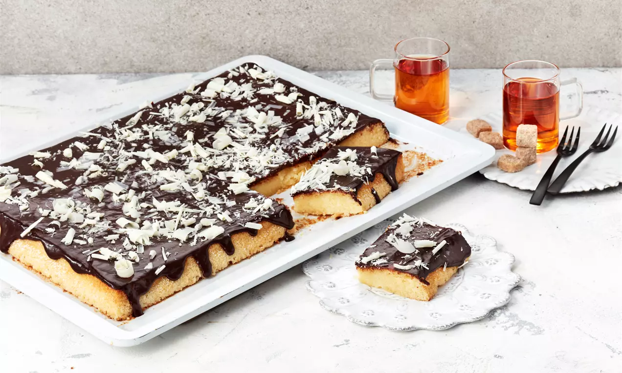 Eierlikörkuchen vom Blech mit saftigem goldgelbem Teig und dunklem, glänzendem Schokoladenguss, in Stücke geschnitten auf Backblech