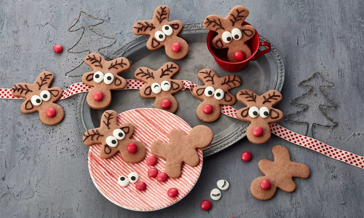 Rentier-Plätzchen auf Holzbrett: braune Lebkuchen-Kekse mit Zuckeraugen, roten Smarties-Nasen und Schokogeweihen, dekorativ angerichtet