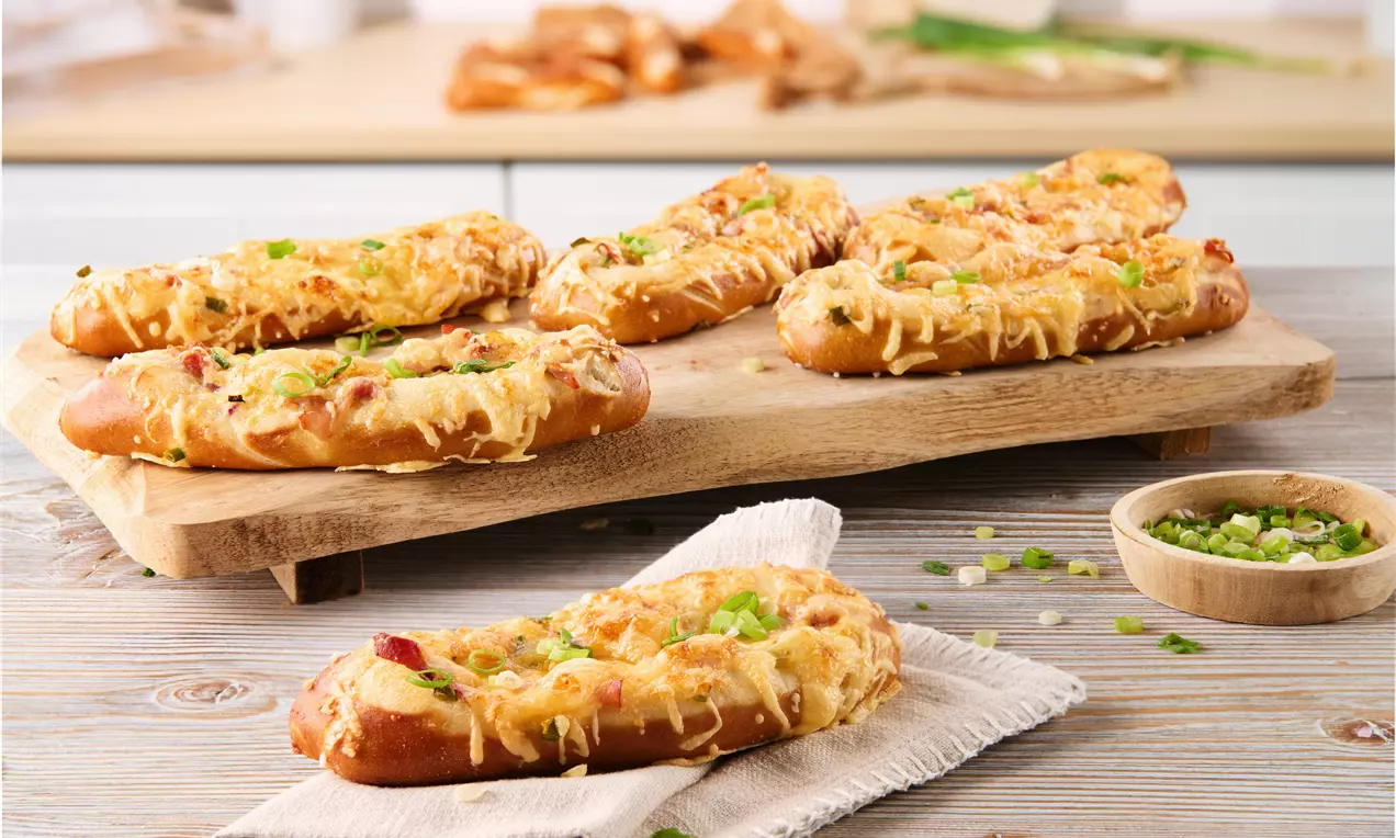 Gefüllte goldbraune Laugenstangen mit geschmolzenem Käse, knusprigem Belag und Frühlingszwiebeln auf rustikalem Holzbrett drapiert