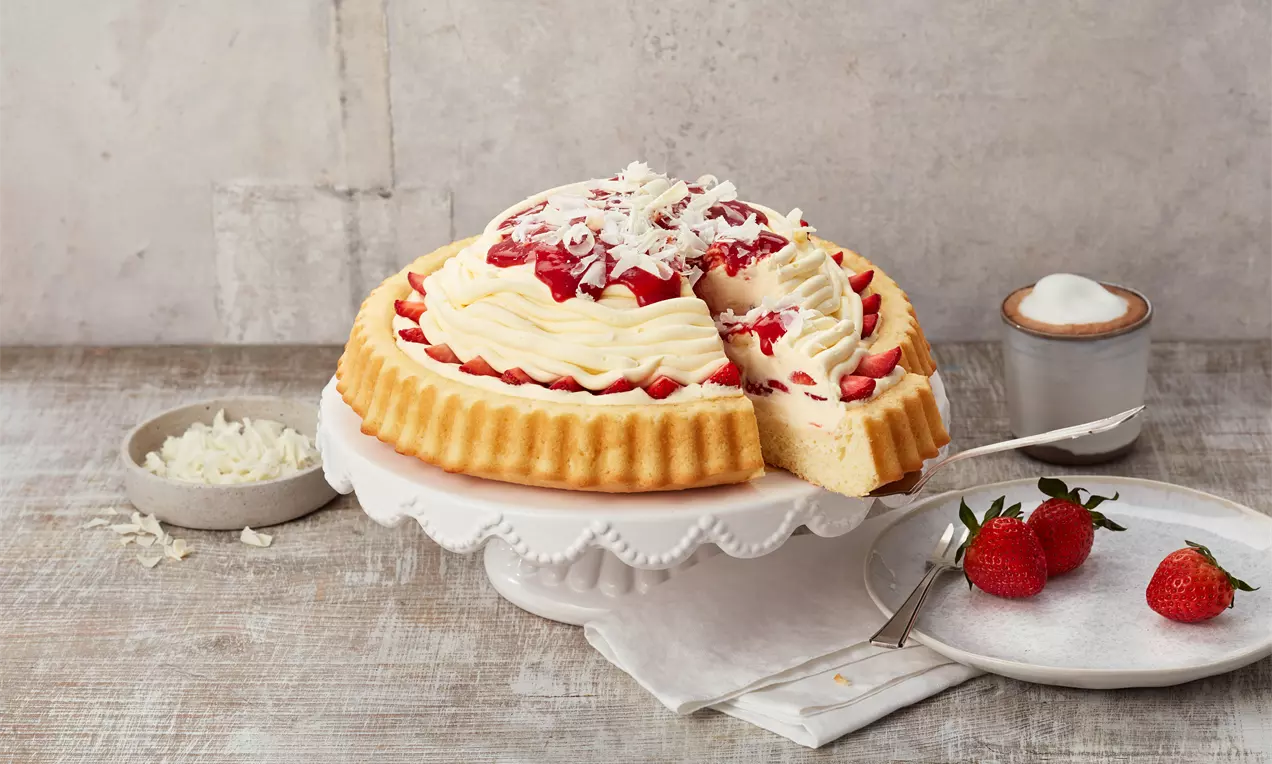 Spaghetti-Eis-Kuchen mit weißer Sahnecreme, roten Erdbeersoßen-Tupfen, weißen Schokoraspeln auf gewelltem Boden auf weißer Tortenplatte