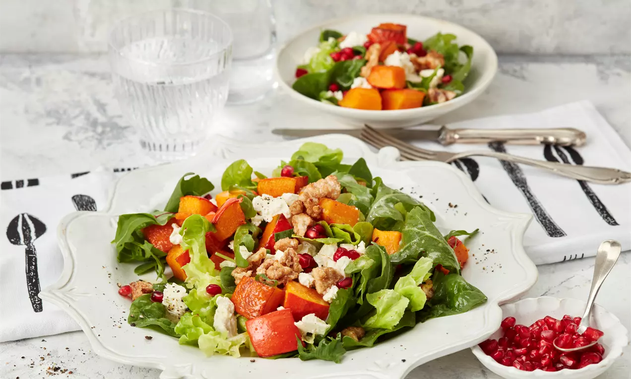 Kürbissalat mit goldenen gerösteten Kürbiswürfeln, Rucola, Feta, Walnüssen und Granatapfelkernen auf hellem Teller