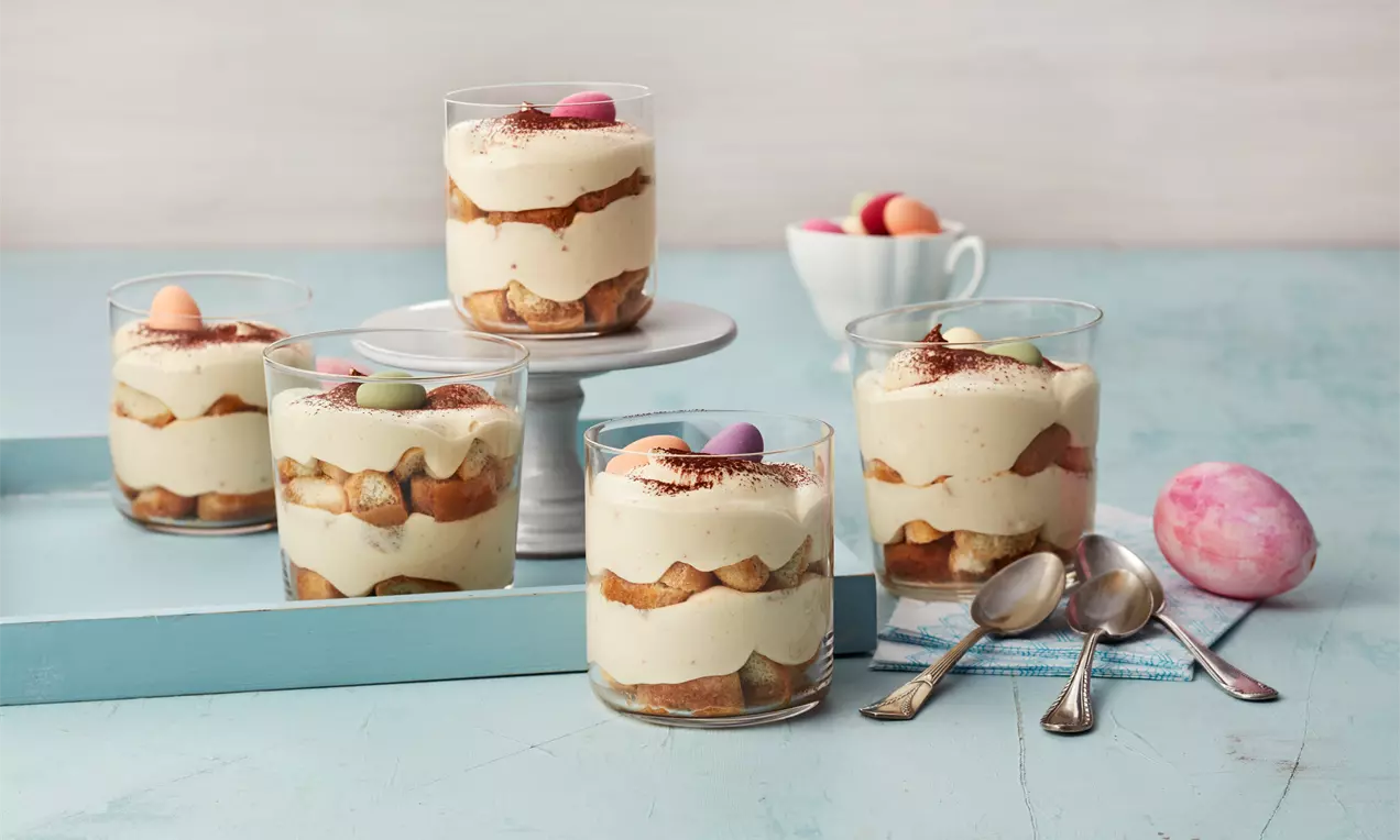 Eierlikör-Tiramisu im klaren, niedrigen Glas mit Schichten aus cremefarbener Creme, hellbrauen Löffelbiskuits und bunten Schokoladeneiern