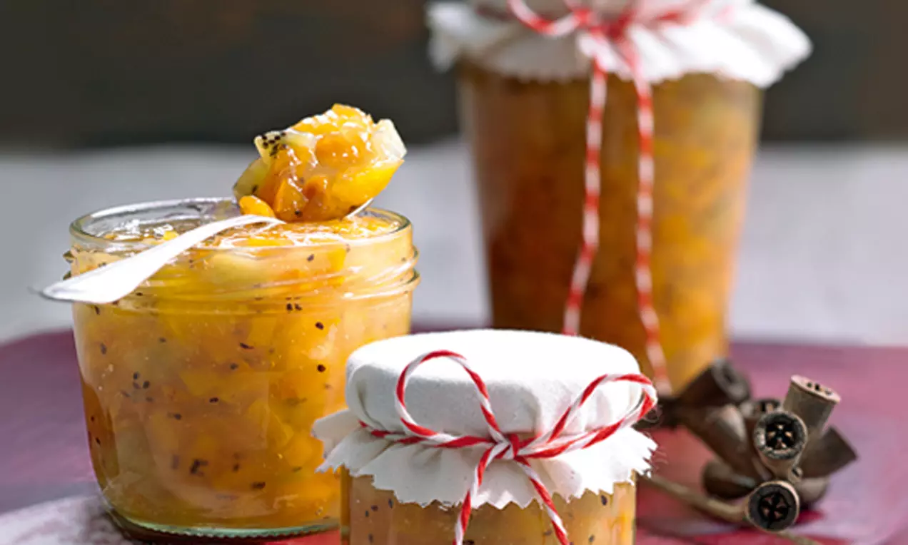 Goldorange Kaki-Orangen-Konfitüre mit feinen Ingwerstückchen, in Gläsern mit Stoffdeckeln und rotem Band auf hellem Untergrund drapiert