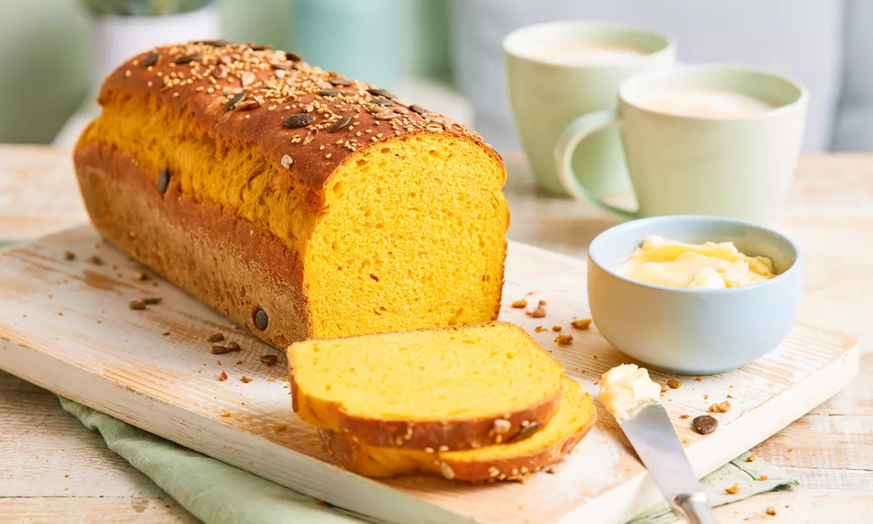 Kürbis-Stuten mit leuchtend orangefarbener, luftiger Krume und dunkler Kruste, serviert auf Holzbrett mit Butter und Messer