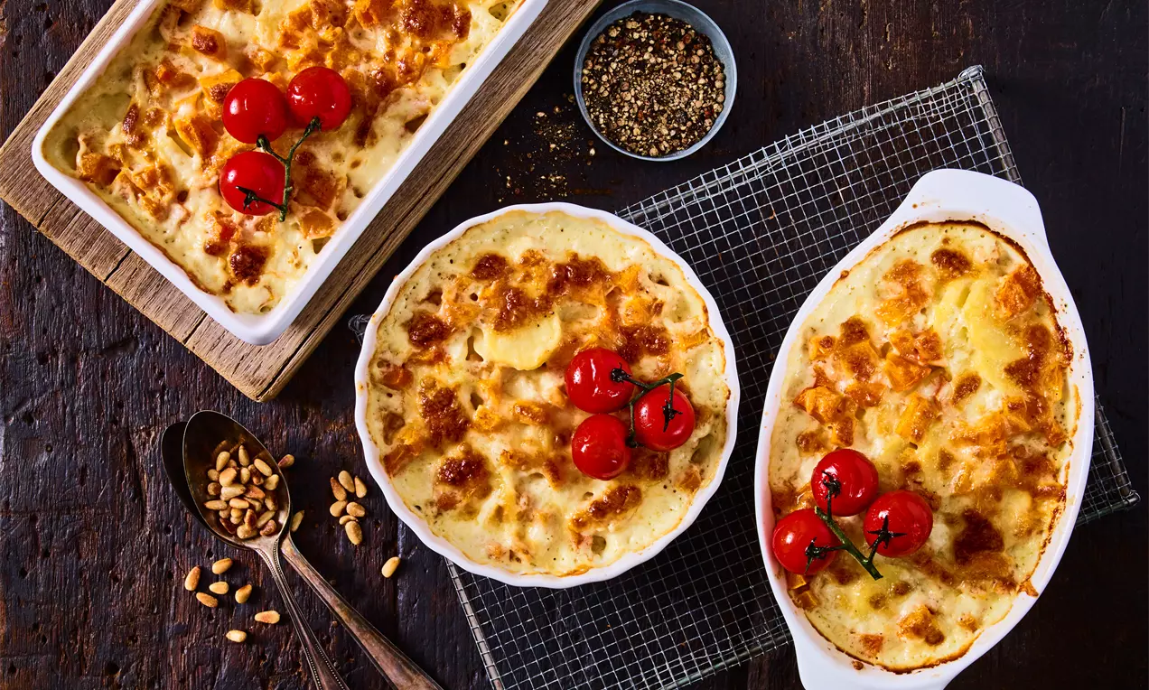 Goldbrauner Kürbis-Kartoffel-Auflauf mit knuspriger Käsekruste, garniert mit glänzenden roten Cocktailtomaten auf rustikalem Holztisch