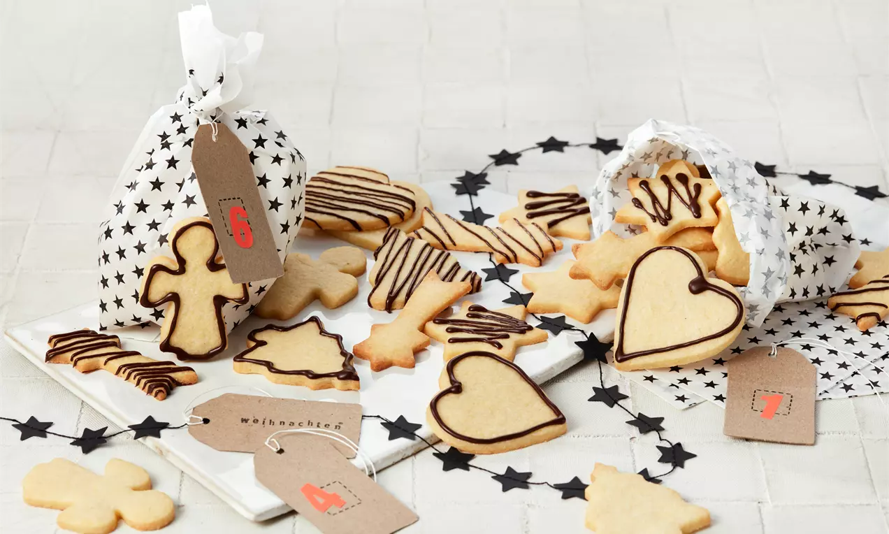 Mürbeteig-Plätzchen in Herz-, Tannenbaum- und Kreuzform, teils mit dunkler Schokoglasur verziert, auf hellem Untergrund arrangiert