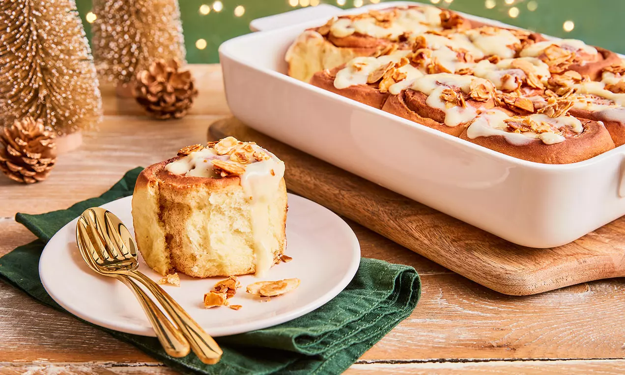 Weihnachtliche Zimtschnecken mit weißem Frischkäsetopping, goldbraun gebacken, mit Zimt bestäubt und auf Holzbrett angerichtet