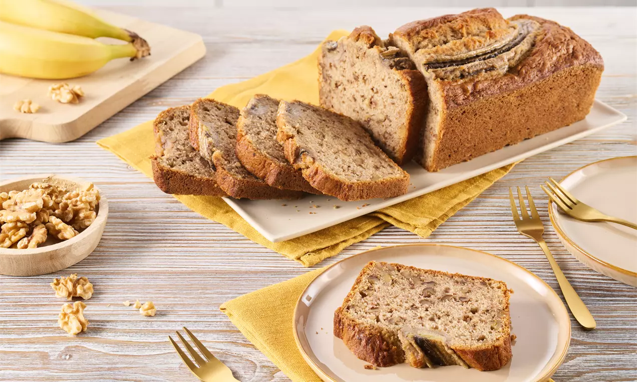 Saftiges, goldbraun gebackenes Bananenbrot mit eingeschnittenen Bananenscheiben, in Scheiben geschnitten auf einem rechteckigen Teller angerichtet