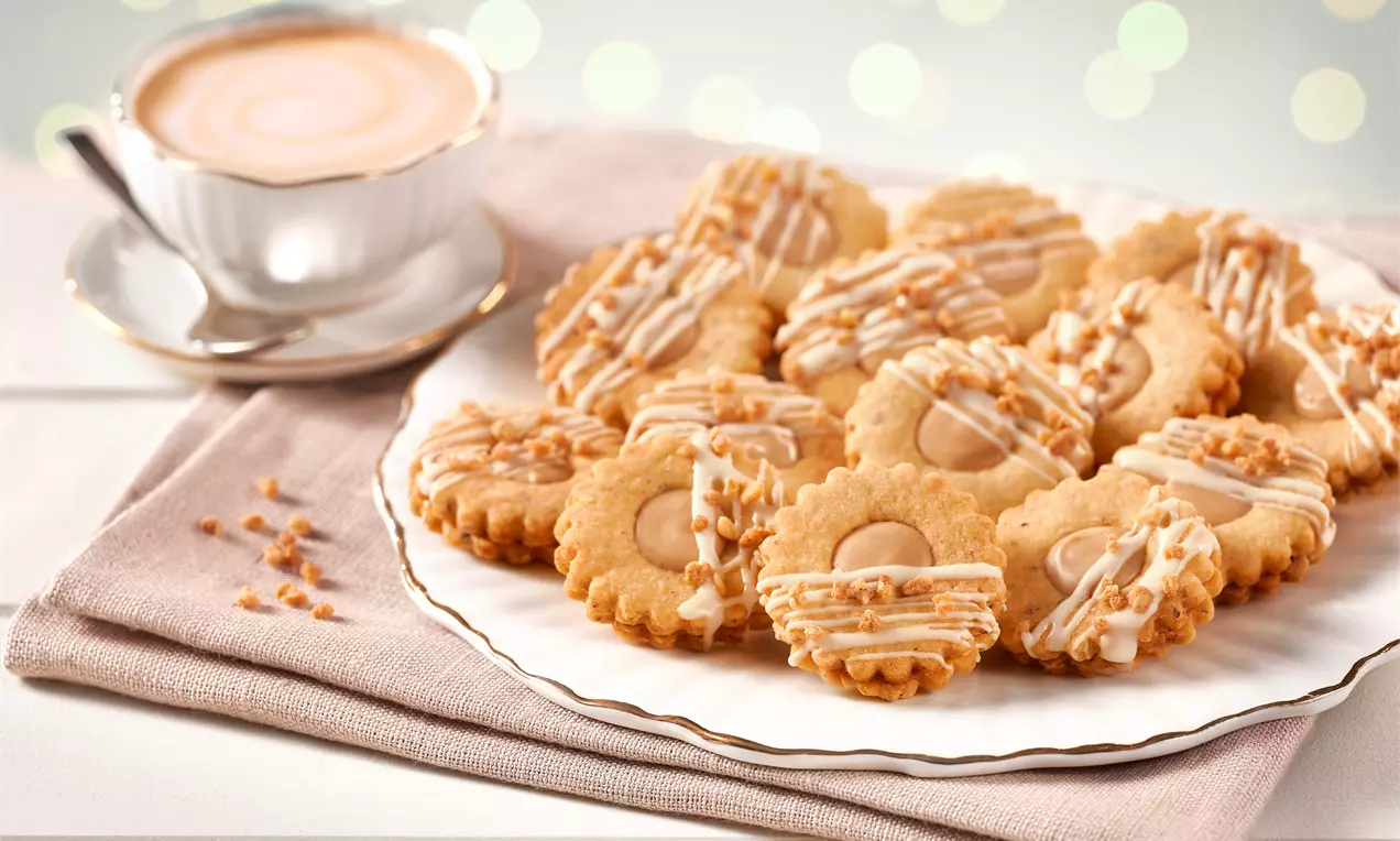 Gefüllte Haselnuss-Plätzchen mit goldbrauner Oberfläche, zarter Glasur und gehackten Nüssen kunstvoll arrangiert auf weißem Teller