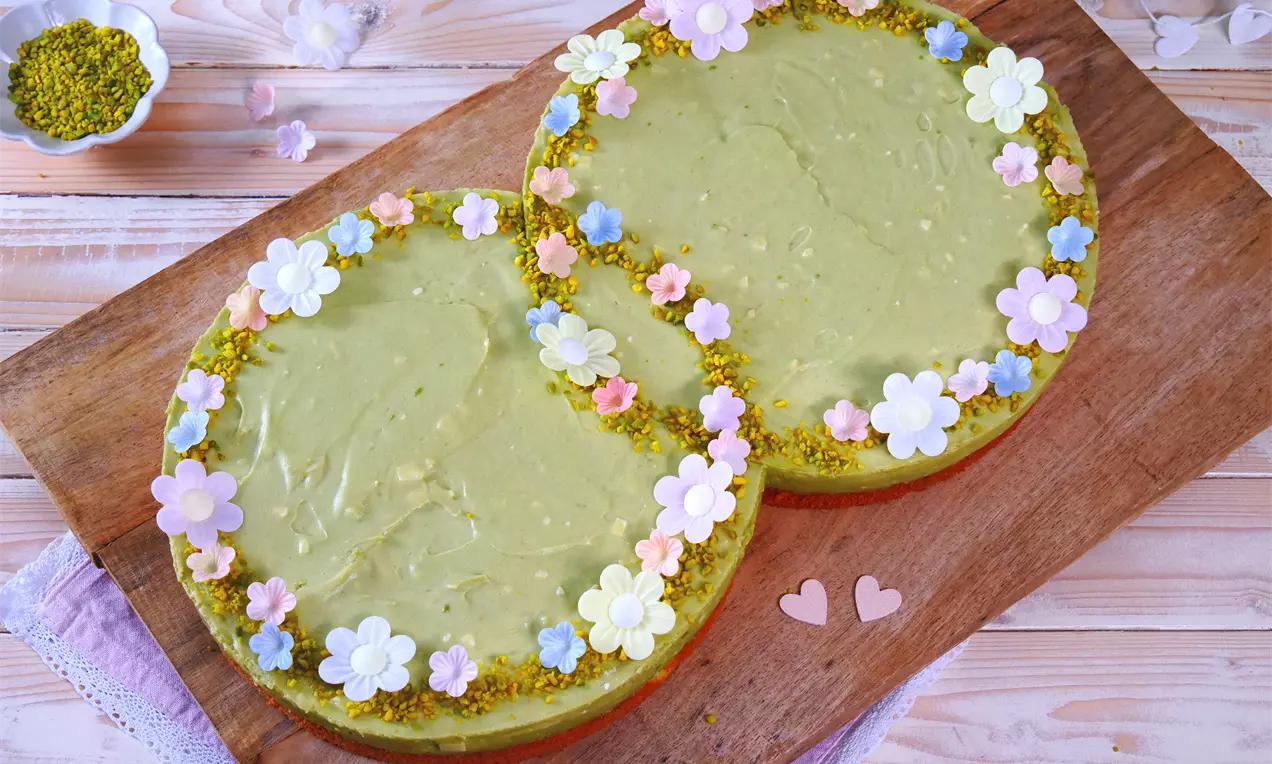 Grüne Hochzeitstorte in Doppeloptik mit cremiger Oberfläche, verziert mit bunten Esspapier-Blumen und Pistazien auf Holzbrett